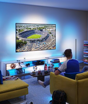 Suasana nobar pertandingan sepak bola di ruang keluarga menggunakan Philips Smart Lighting Connected by WiZ yang menyinkronkan efek cahaya biru di sekitar TV untuk menciptakan pengalaman menonton yang lebih imersif.