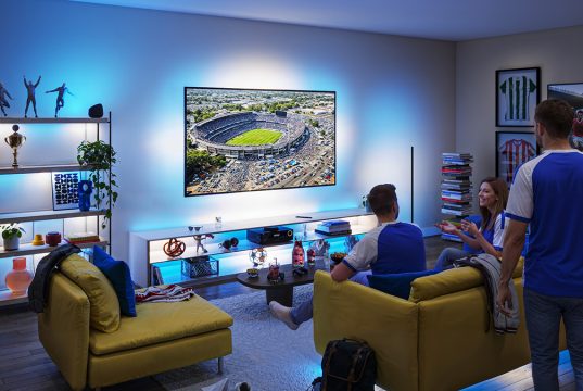 Suasana nobar pertandingan sepak bola di ruang keluarga menggunakan Philips Smart Lighting Connected by WiZ yang menyinkronkan efek cahaya biru di sekitar TV untuk menciptakan pengalaman menonton yang lebih imersif.