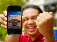 Seorang pria sedang mengangkat smartphone yang emncantumkan program Bagi-Bagi Bahagia Telkomsel