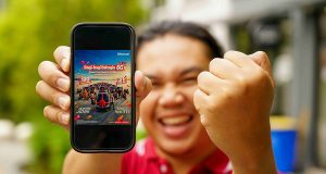 Telkomsel Bagi-Bagi Bahagia, Siapkan 31 Mobil BYD M6 EV dan 120 Motor Yamaha NMAX Seorang pria sedang mengangkat smartphone yang emncantumkan program Bagi-Bagi Bahagia Telkomsel