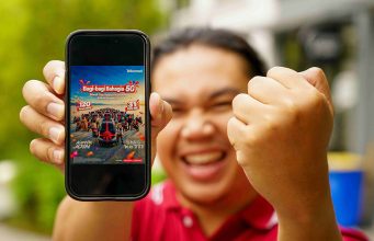 Seorang pria sedang mengangkat smartphone yang emncantumkan program Bagi-Bagi Bahagia Telkomsel