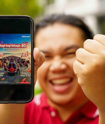 Telkomsel Bagi-Bagi Bahagia, Siapkan 31 Mobil BYD M6 EV dan 120 Motor Yamaha NMAX Seorang pria sedang mengangkat smartphone yang emncantumkan program Bagi-Bagi Bahagia Telkomsel