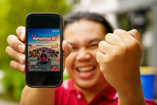 Seorang pria sedang mengangkat smartphone yang emncantumkan program Bagi-Bagi Bahagia Telkomsel