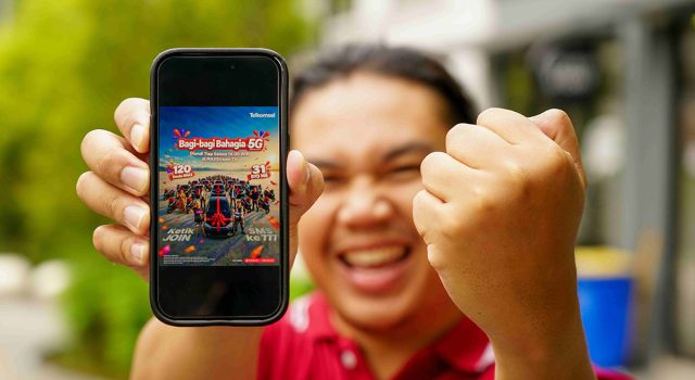 Seorang pria sedang mengangkat smartphone yang emncantumkan program Bagi-Bagi Bahagia Telkomsel