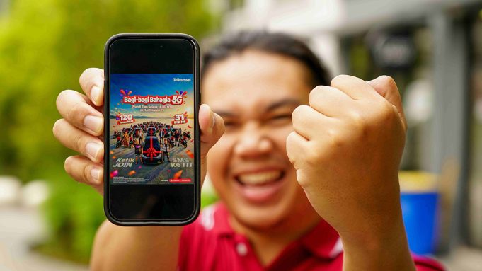 Seorang pria sedang mengangkat smartphone yang emncantumkan program Bagi-Bagi Bahagia Telkomsel