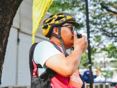 Petugas Jakarta Running Festival 2026 mengenakan helm sepeda dan rompi merah muda sambil menggunakan radio komunikasi Hytera untuk mendukung koordinasi selama ajang lari.