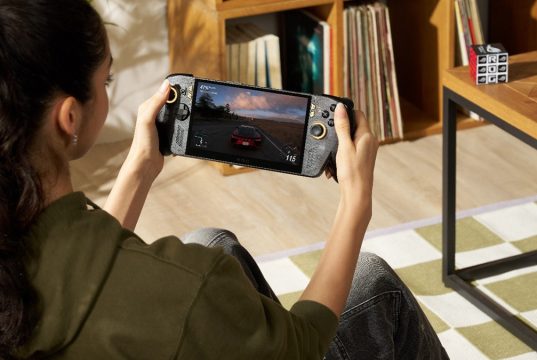 Seorang gamer memainkan ROG XBOX Ally X20, handheld gaming PC edisi 20 tahun ROG, sambil menikmati game balap dengan desain perangkat hitam beraksen emas.
