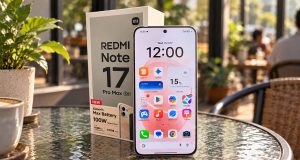 Redmi Note 17 Pro Max 5G dan kotak kemasannya di atas meja kaca bundar bertekstur di kafe dengan pencahayaan alami pagi hari, nuansa warna Fuji yang hangat, serta latar belakang kafe dengan efek bokeh.
